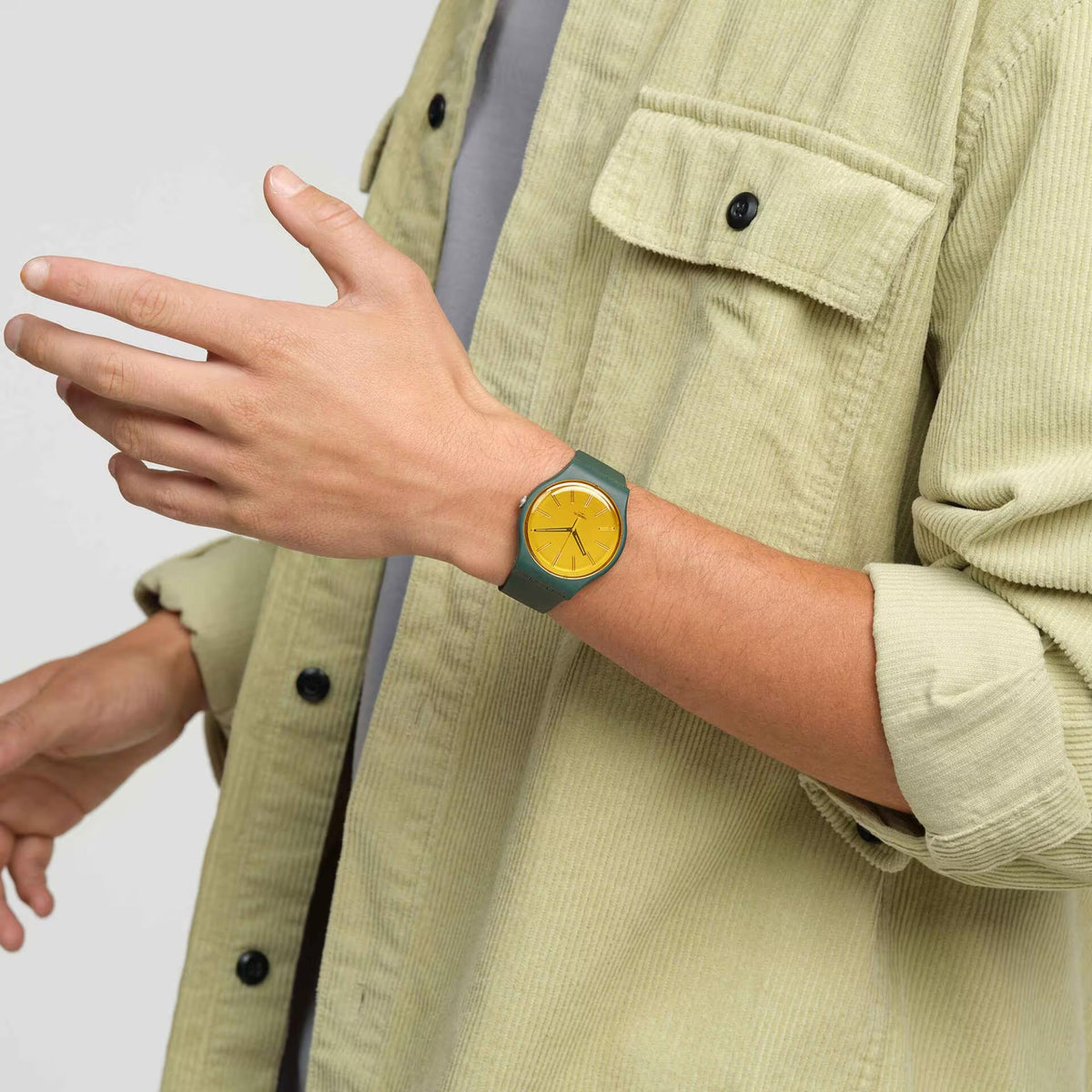 Swatch analog watch on wrist, yellow dial with dark hands and dark green strap