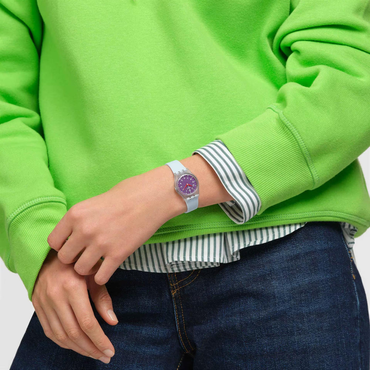Swatch wristwatch on wrist with light blue strap, purple dial detail