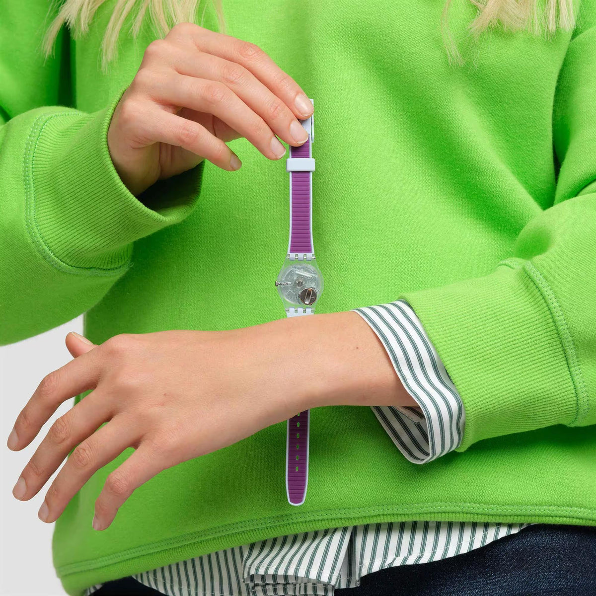 Swatch watch on wrist, purple dial and light blue case with striped band
