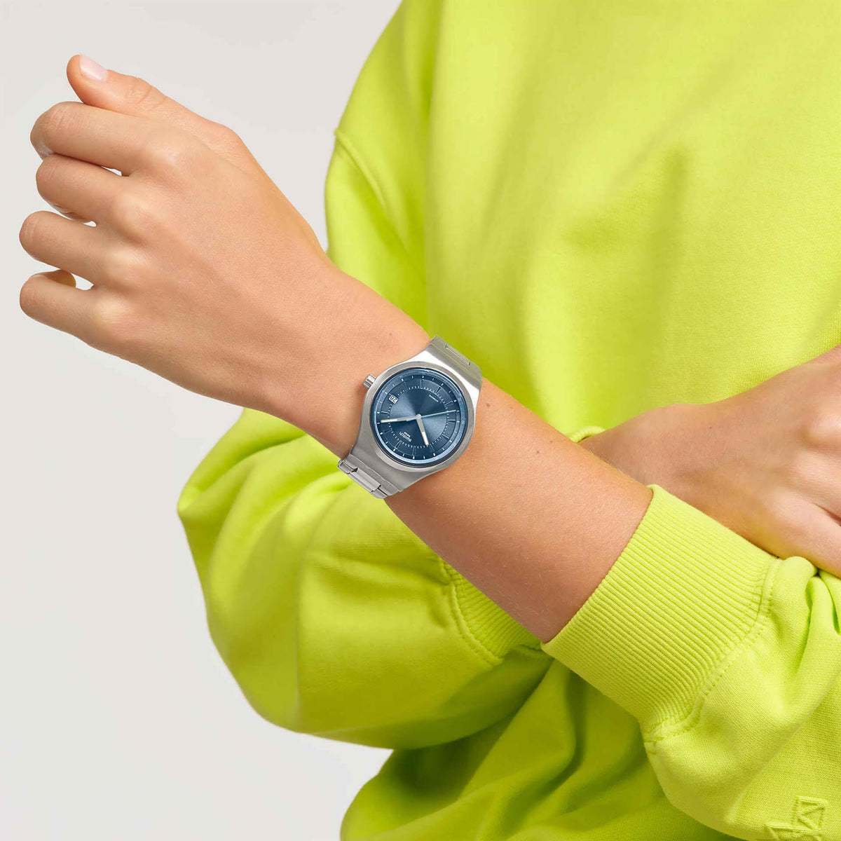 Stainless steel wristwatch on wrist with blue dial and date window; silver crown visible.