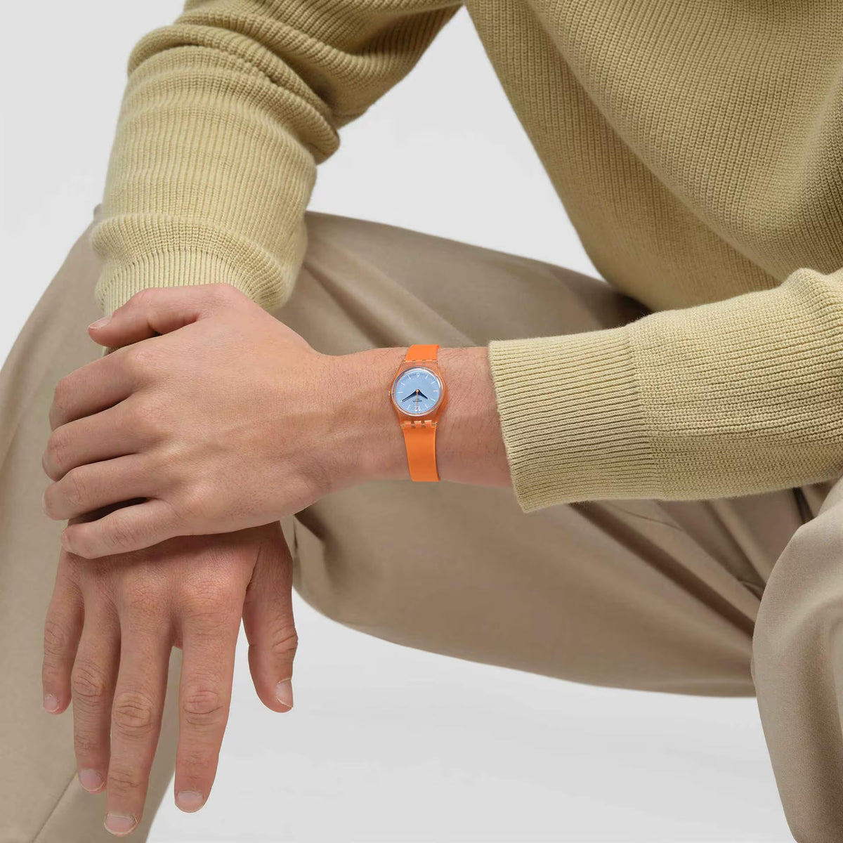 Swatch orange wristwatch with light blue dial on wrist, worn with beige knit sleeves