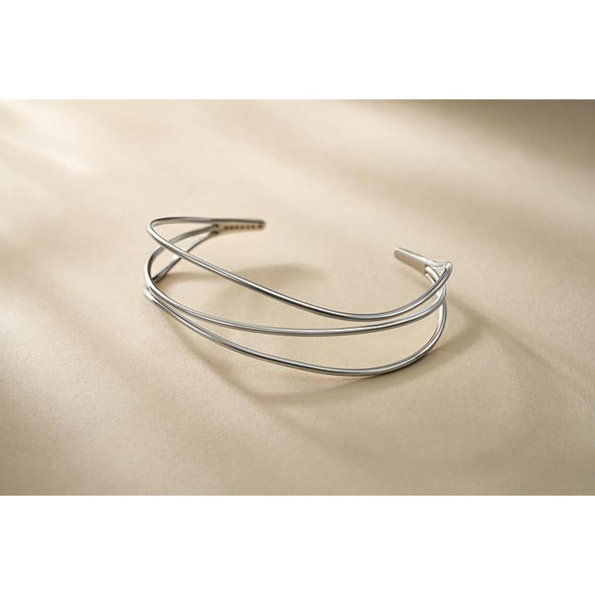 Silver-tone wire bracelet with three stacked curved bands, open cuff on light background