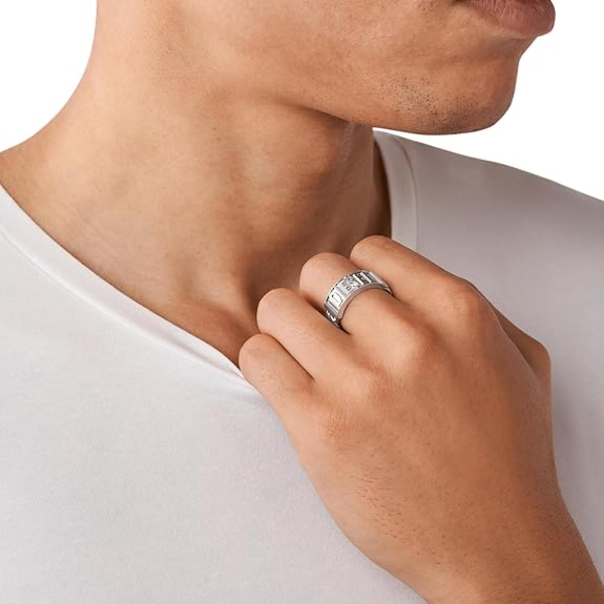 Stainless steel DIESEL logo ring worn on a man's finger against a white shirt