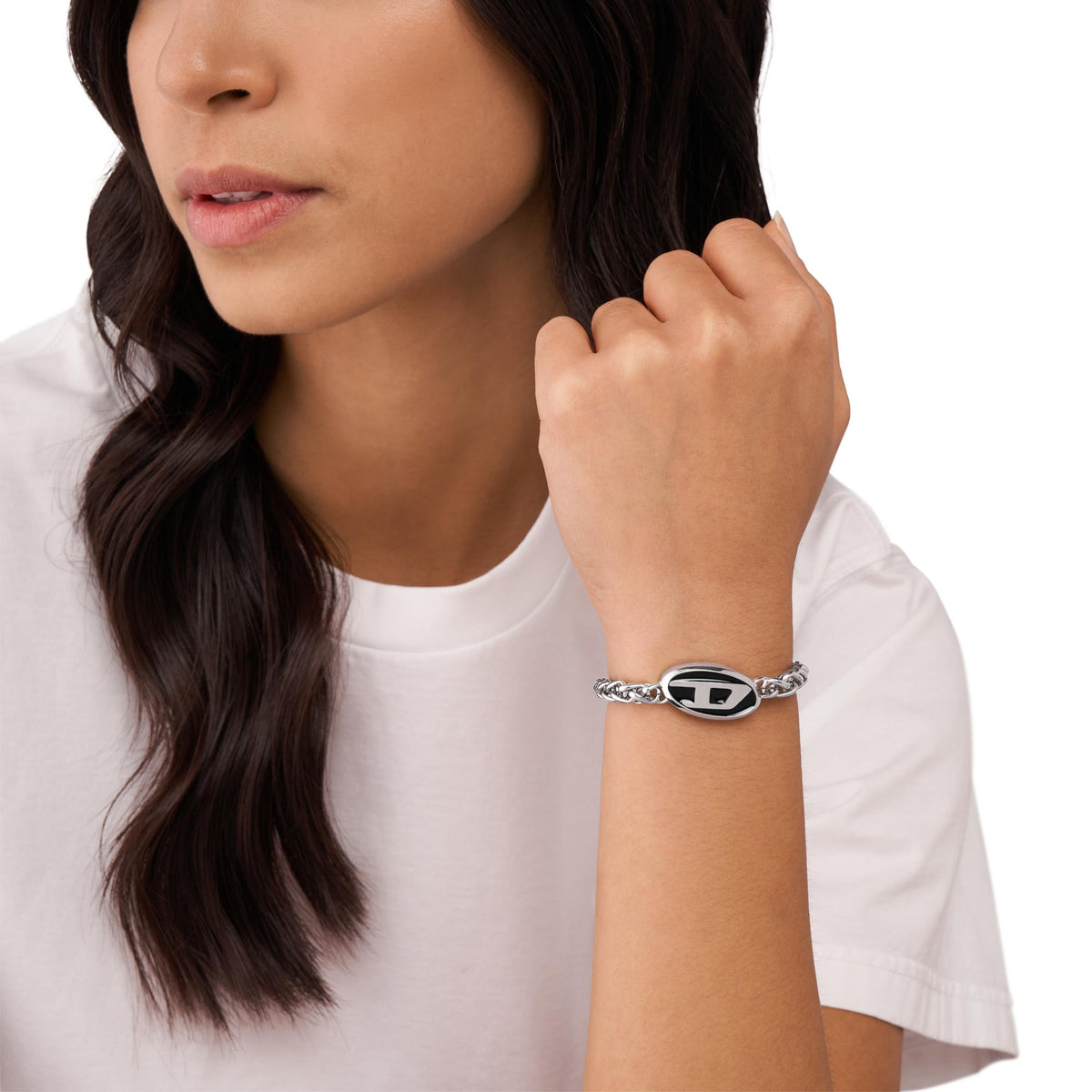 Stainless steel chain bracelet with oval logo charm on wrist, silver tone
