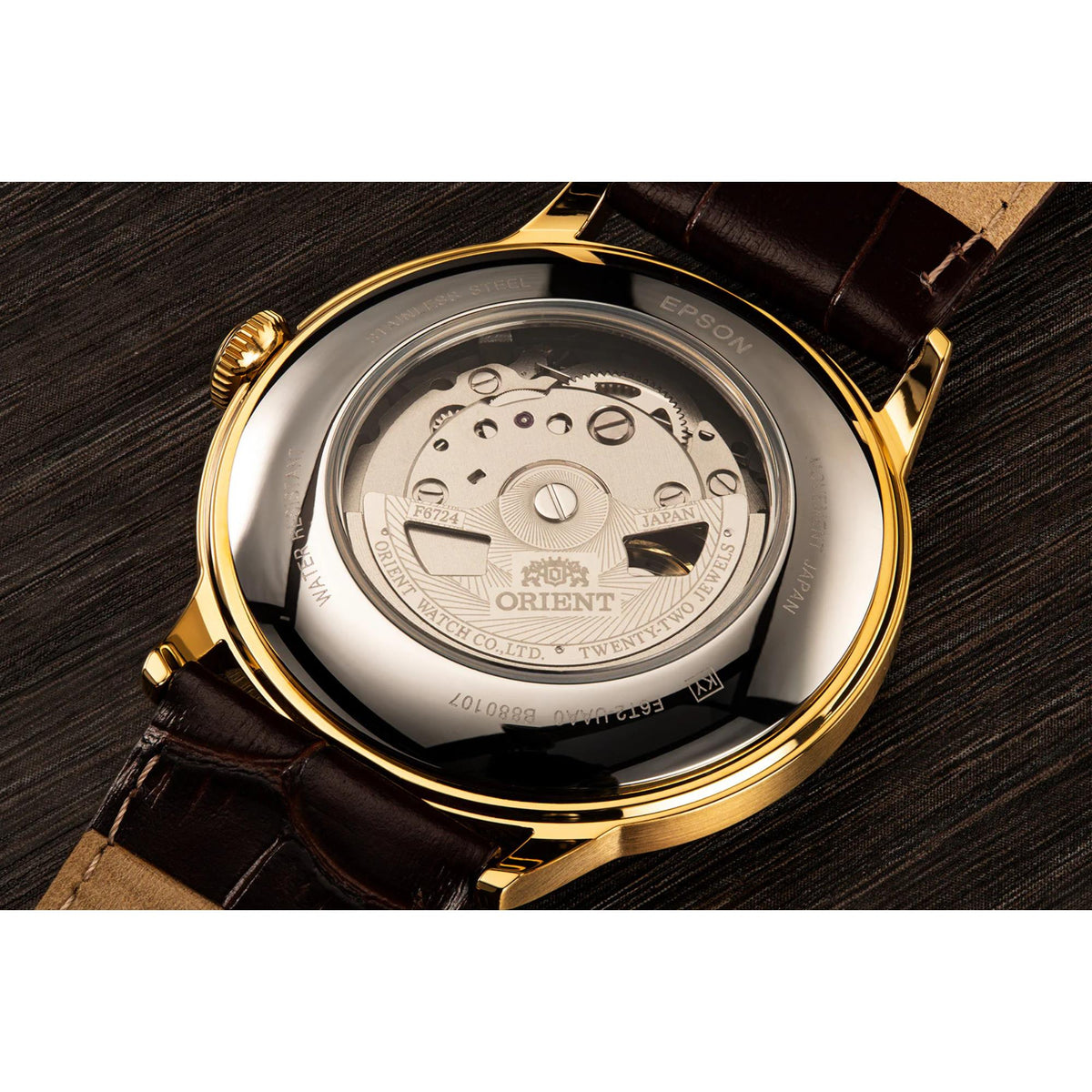 Gold-tone watch case back showing mechanism under crystal, on brown leather strap