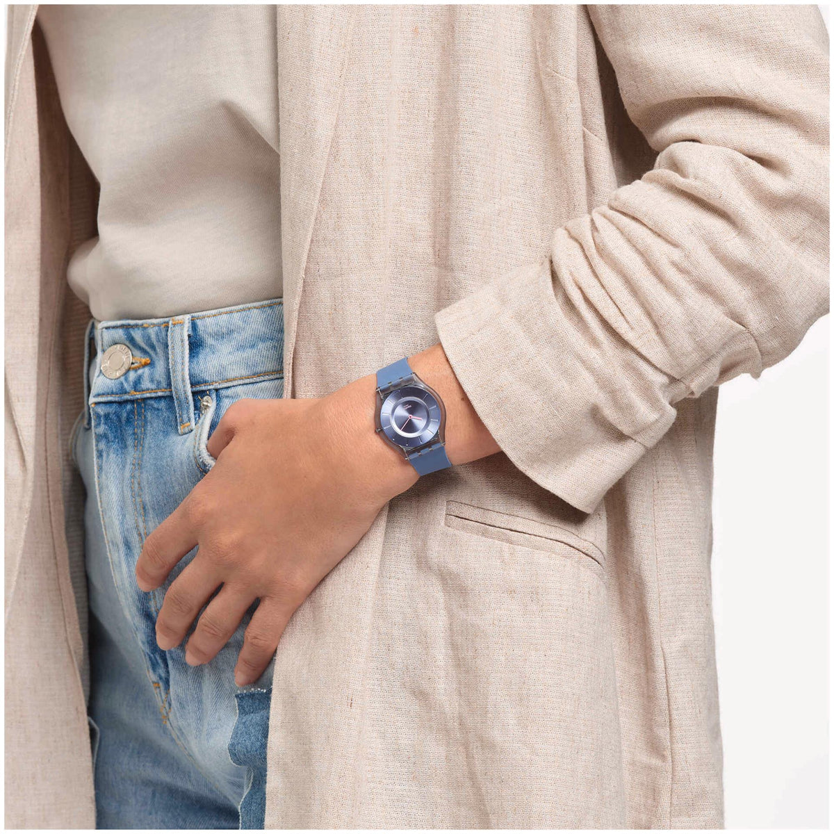 Denim blue Swatch watch on wrist with blue band and round silver dial