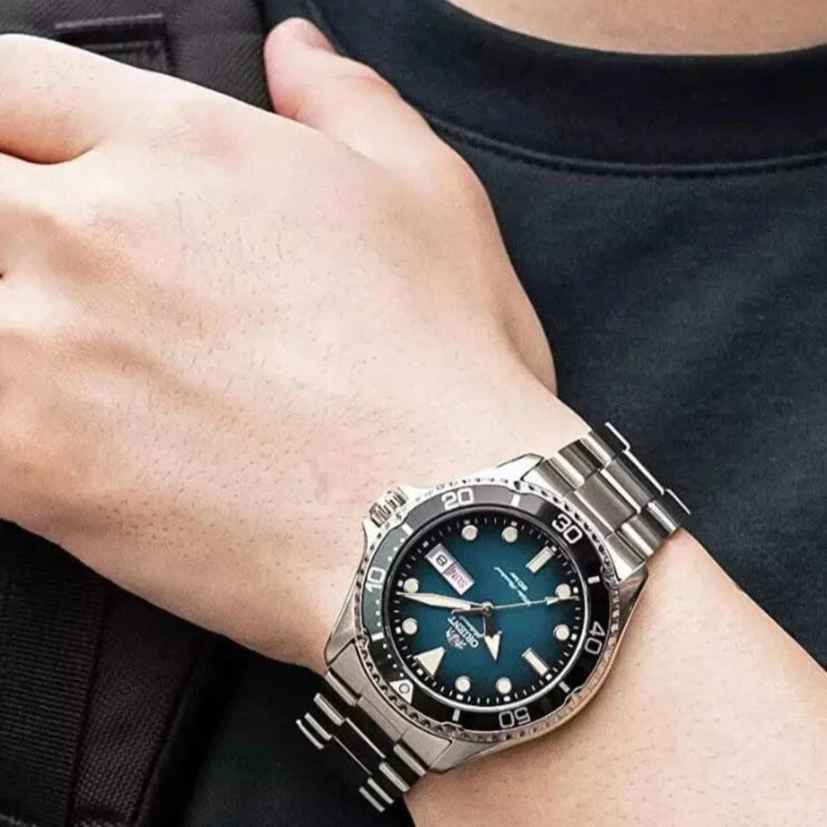 Men's automatic watch worn on wrist with teal-green dial and steel metal band