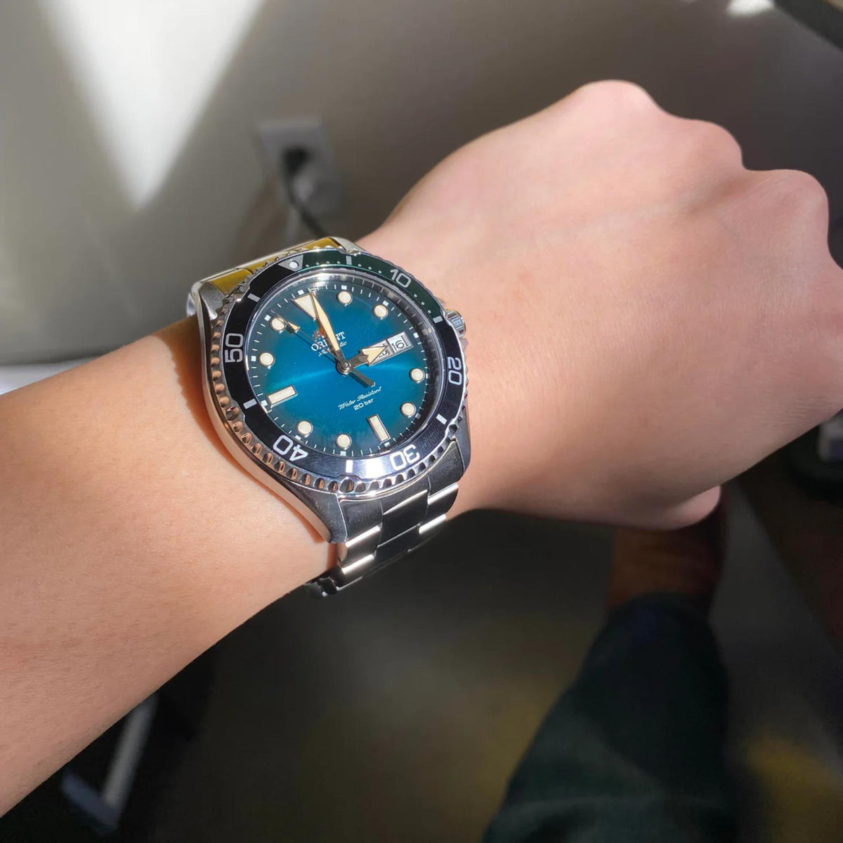 Men's automatic wrist watch with teal-green dial and steel bracelet in side view