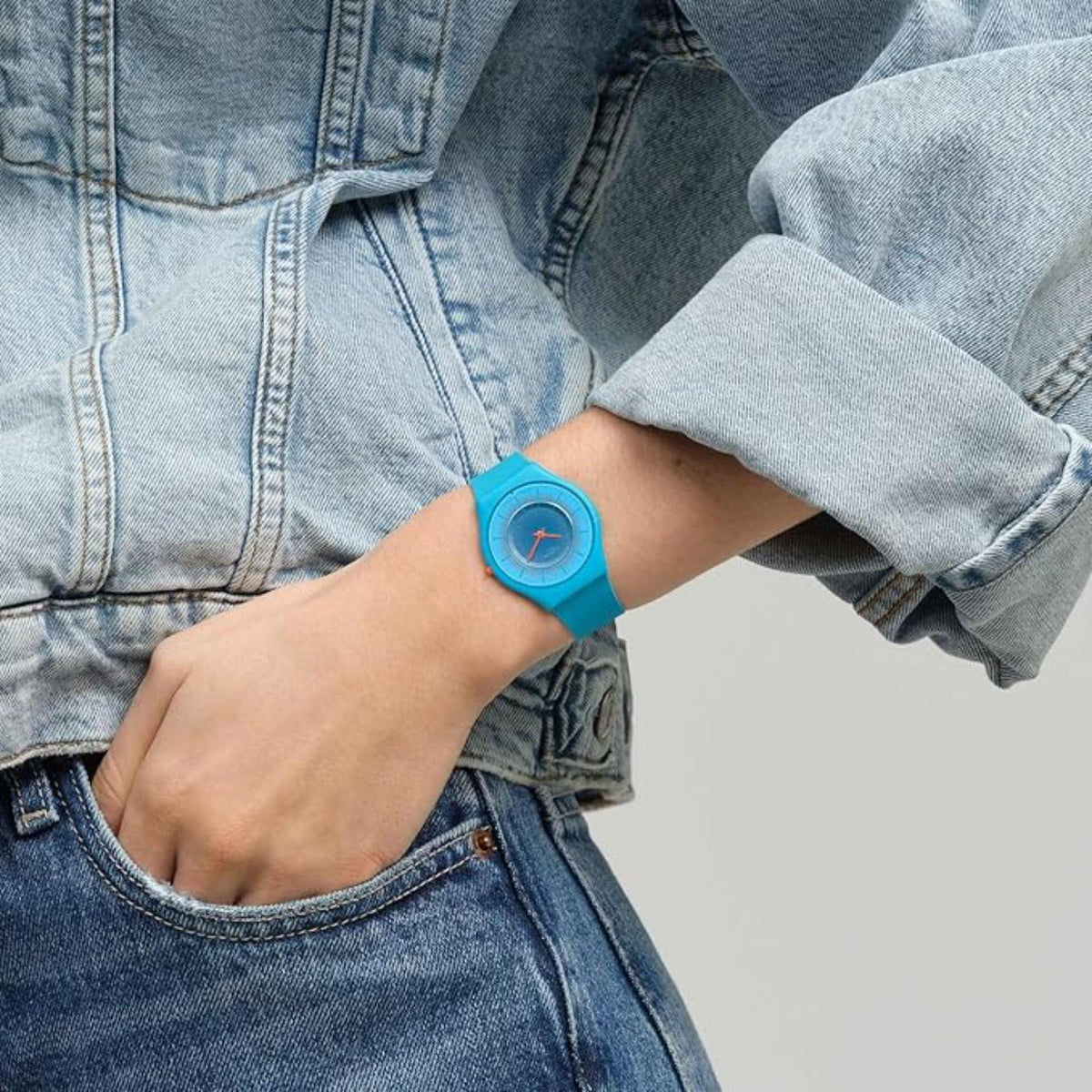 Swatch teal watch on wrist with round blue dial and orange-tipped crown detail