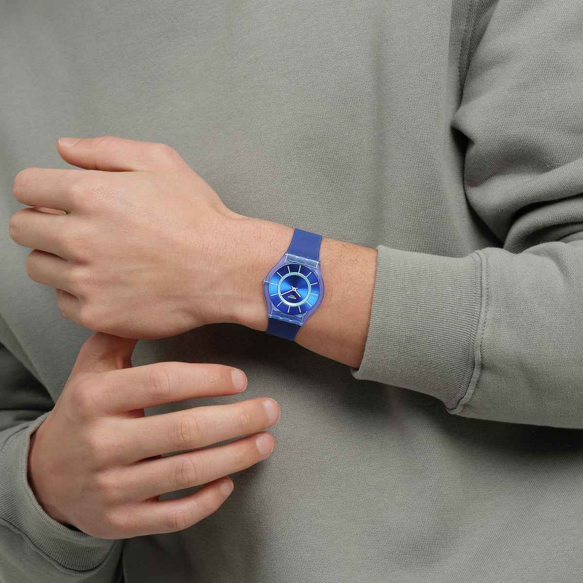 Blue silicone strap Swatch watch on wrist, blue dial with white hour markers and hands