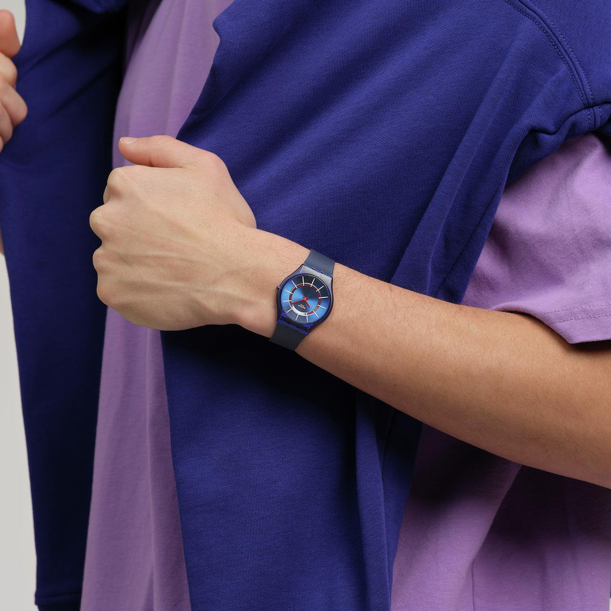 Swatch silicone-strap wristwatch on wrist, blue dial with orange markers and red hands.