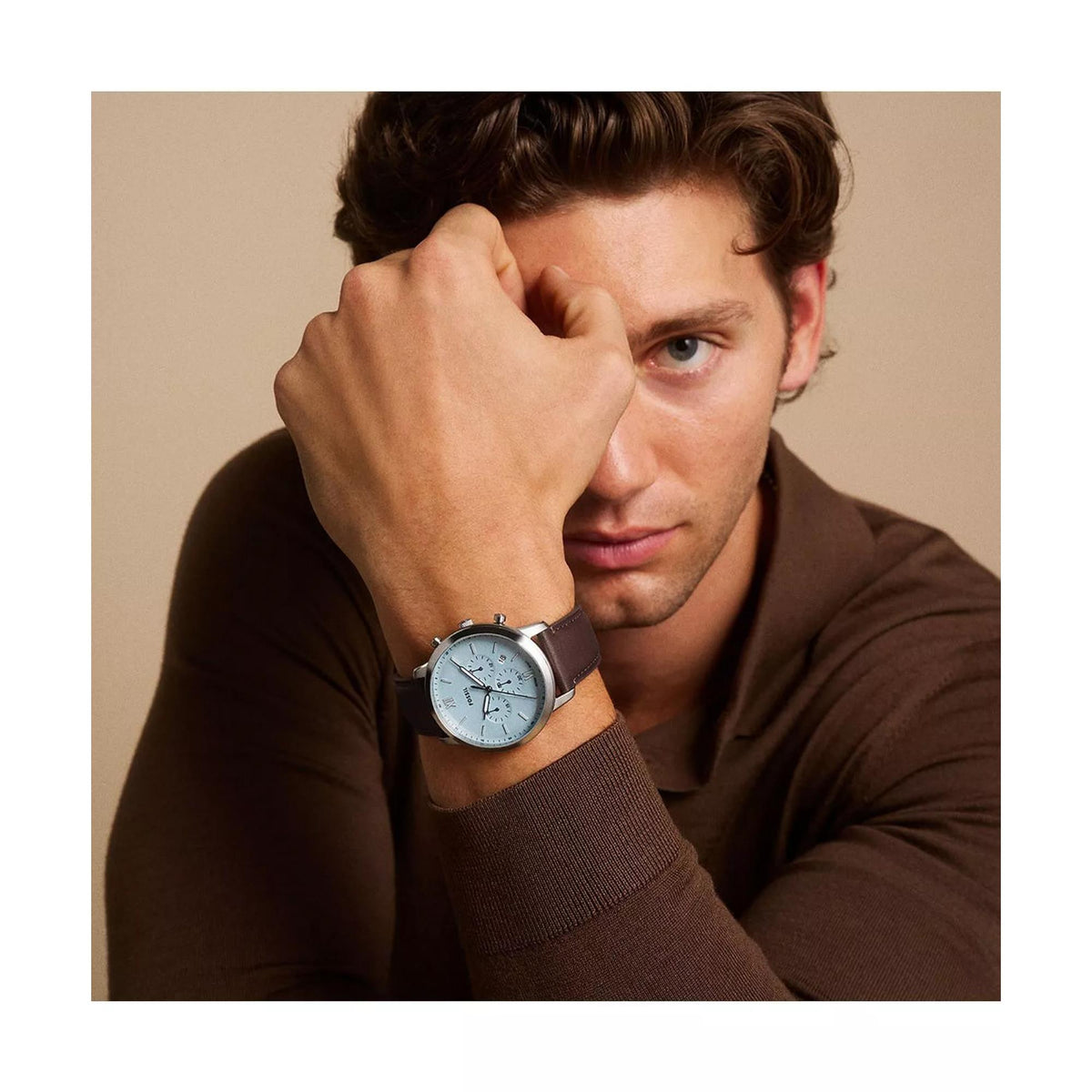 Men's chronograph watch worn on model’s wrist, blue dial, brown leather strap
