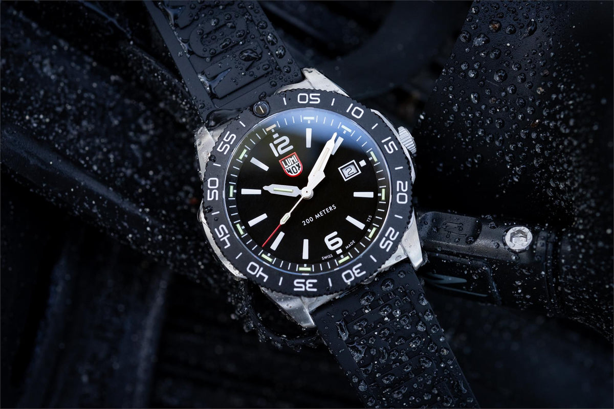 Men's diver watch with black dial and green lume, shown with water droplets on strap.