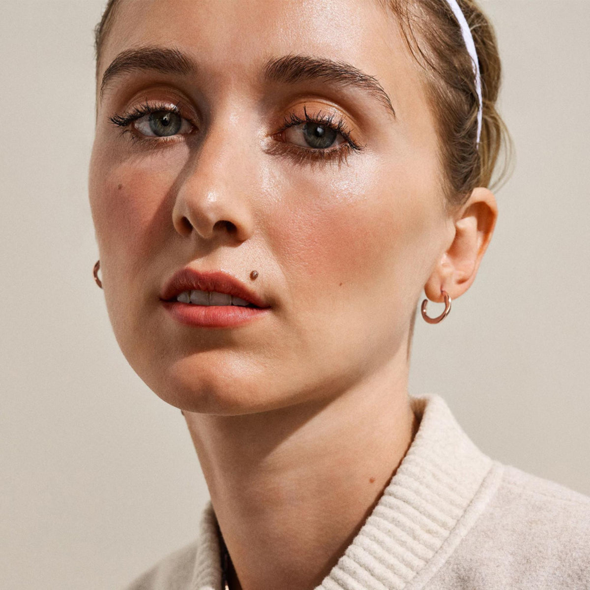 Rose gold-tone hoop earrings on a model, small curved stainless steel hoops