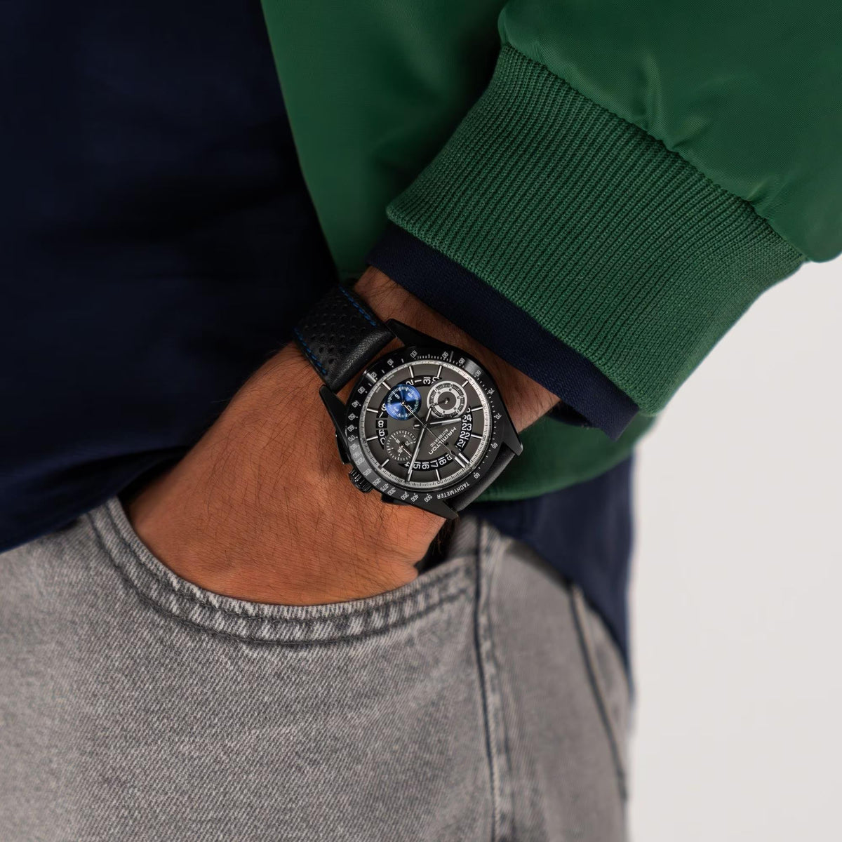Men's chronograph watch on wrist with black perforated leather strap and blue-stitched band