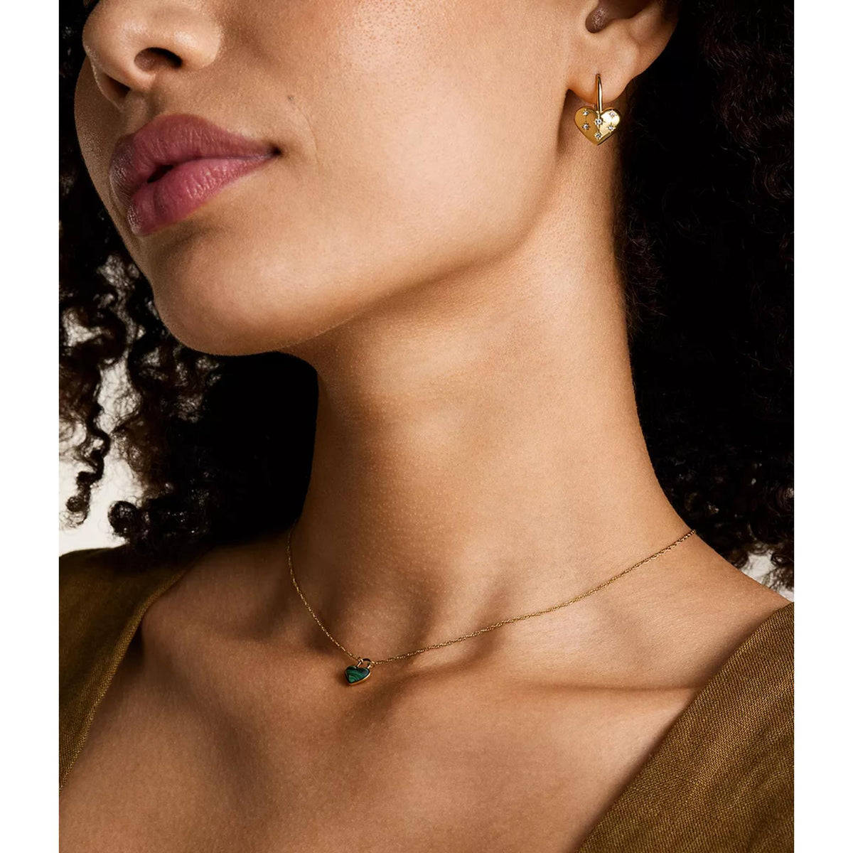 Model wearing gold-tone heart drop earrings with starburst details; hoop backs visible.