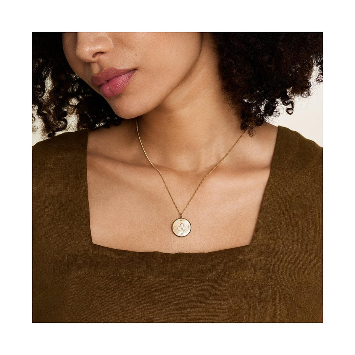 Gold-tone pendant necklace worn on neckline, round mother-of-pearl Leo charm