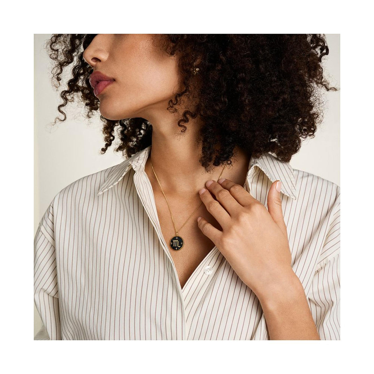 Gold-tone necklace worn; round black starry Scorpio pendant with gold zodiac symbol