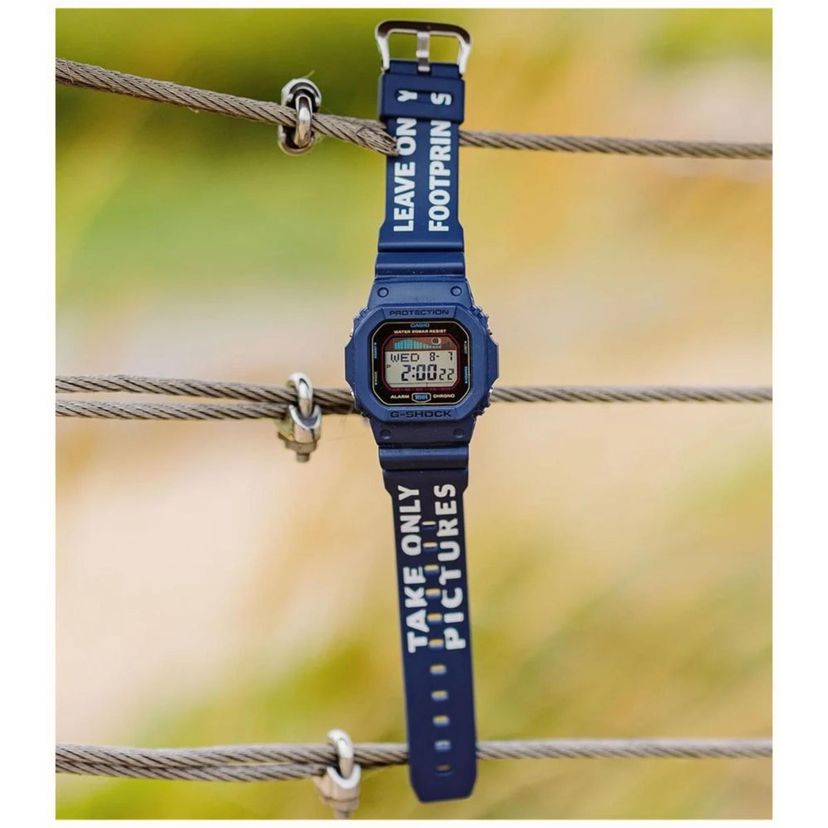 Blue digital watch with motivational text on strap, hanging on a wire with a blurred natural background