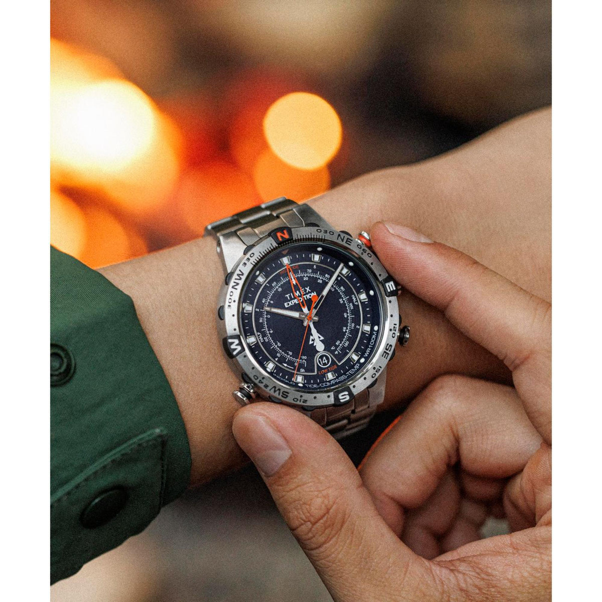 Men's steel quartz watch on wrist with blue dial, orange seconds hand, and metal bracelet