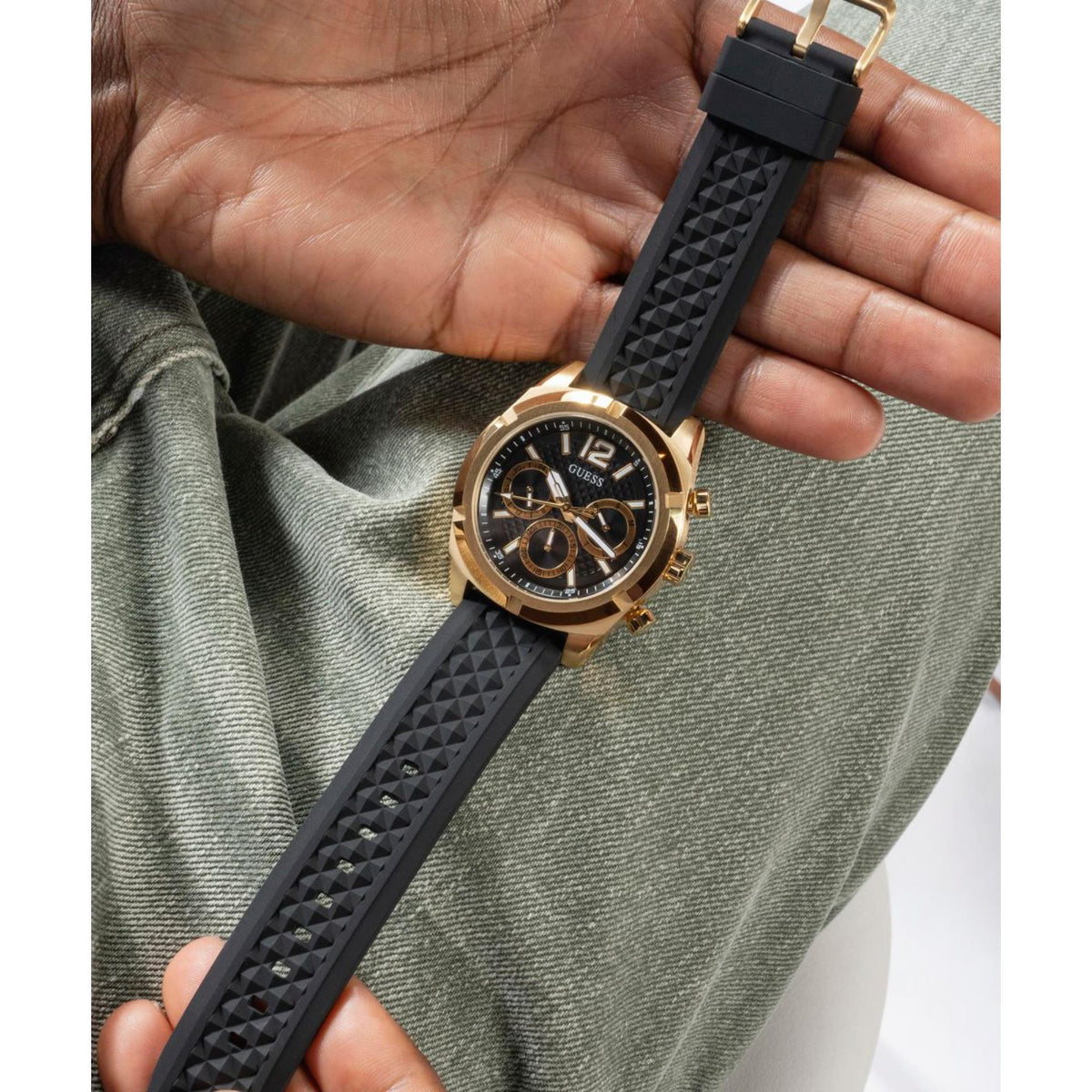 Men's black textured silicone strap and gold-tone chronograph watch face close-up.