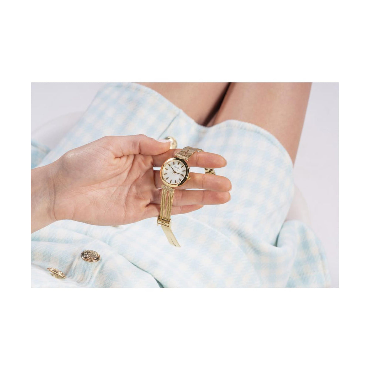 Guess watch held in hand, gold-tone mesh strap and mother-of-pearl dial with crown