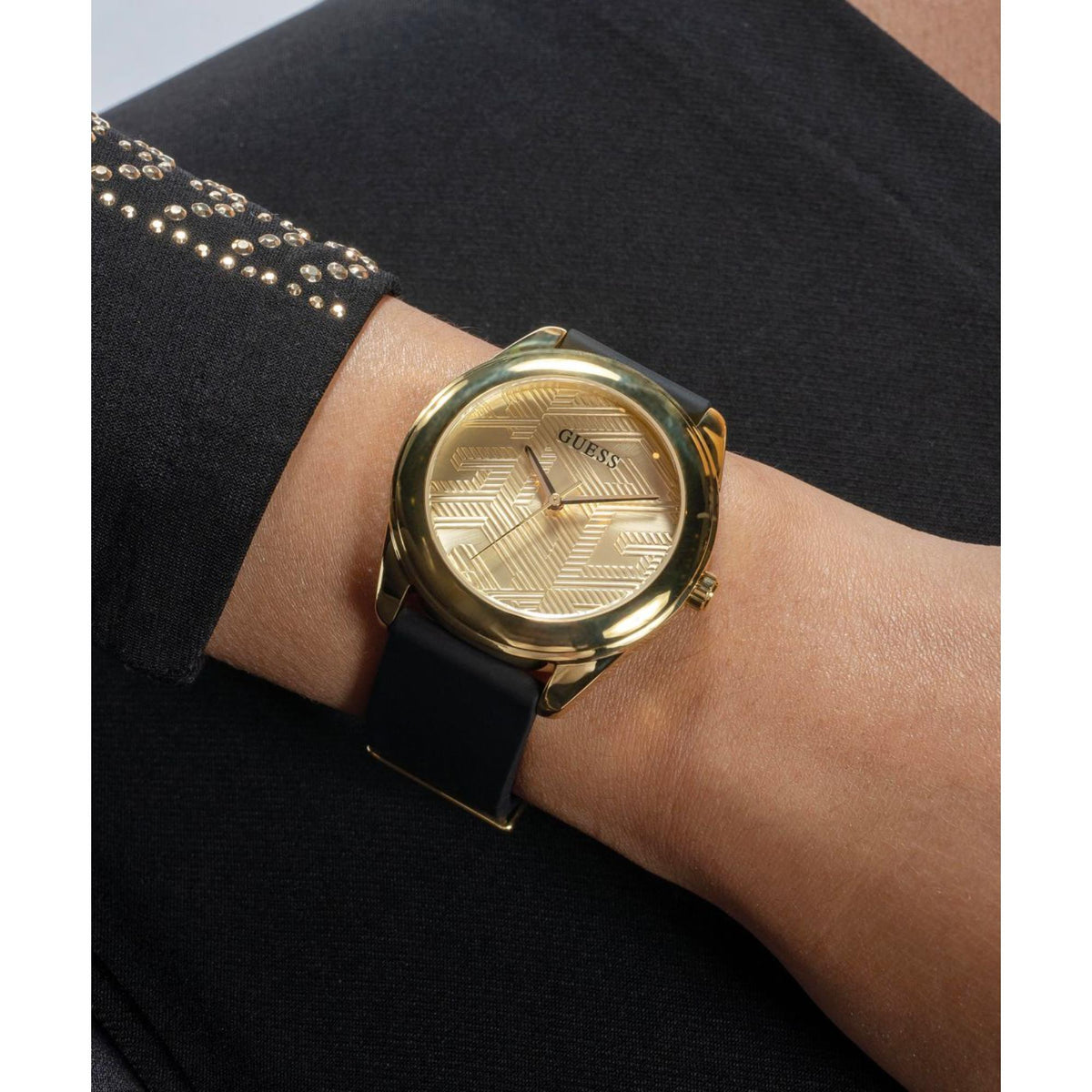 Women's Guess watch on wrist showing gold dial pattern and black silicone strap