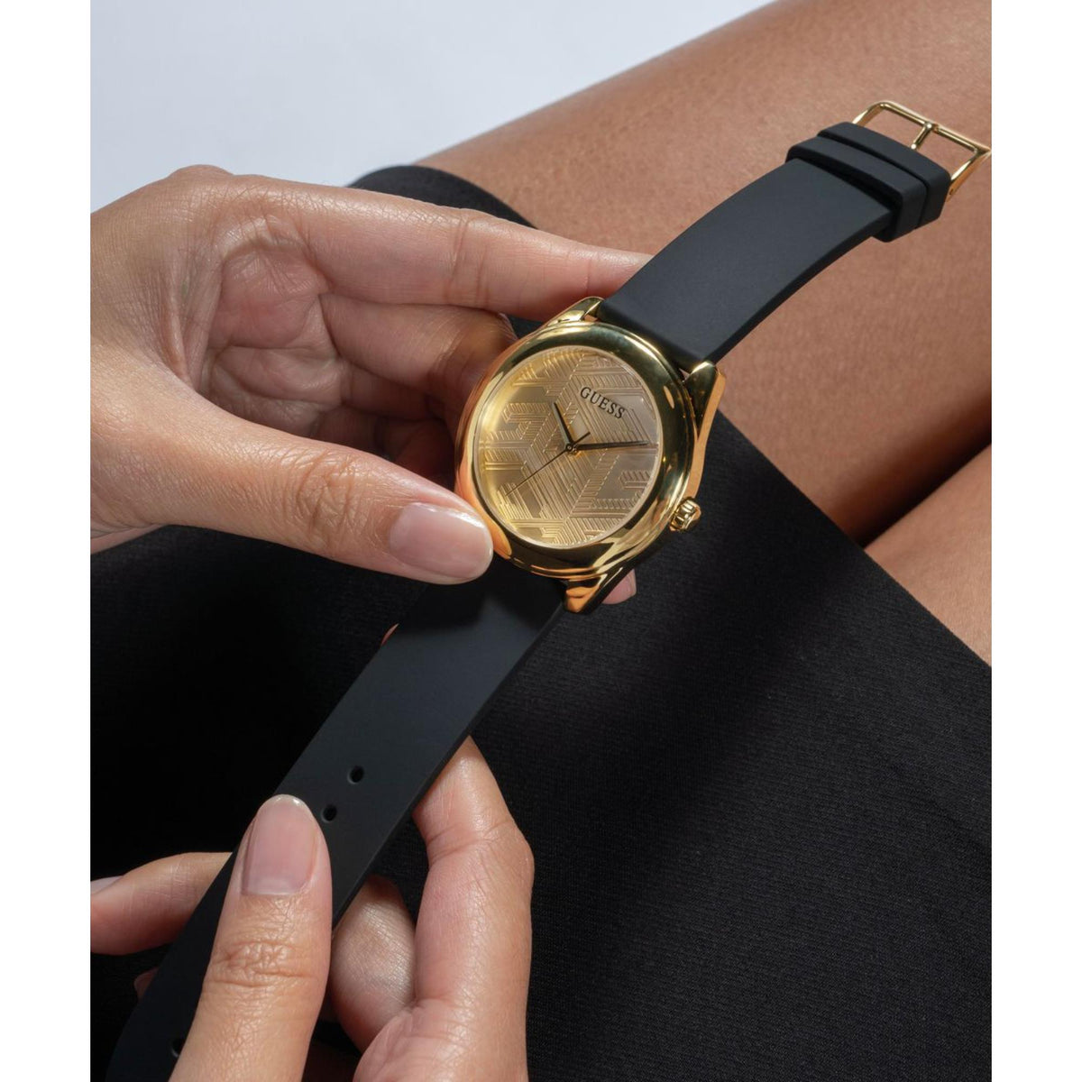Hands adjusting black silicone strap on a gold-tone Guess watch with gold dial