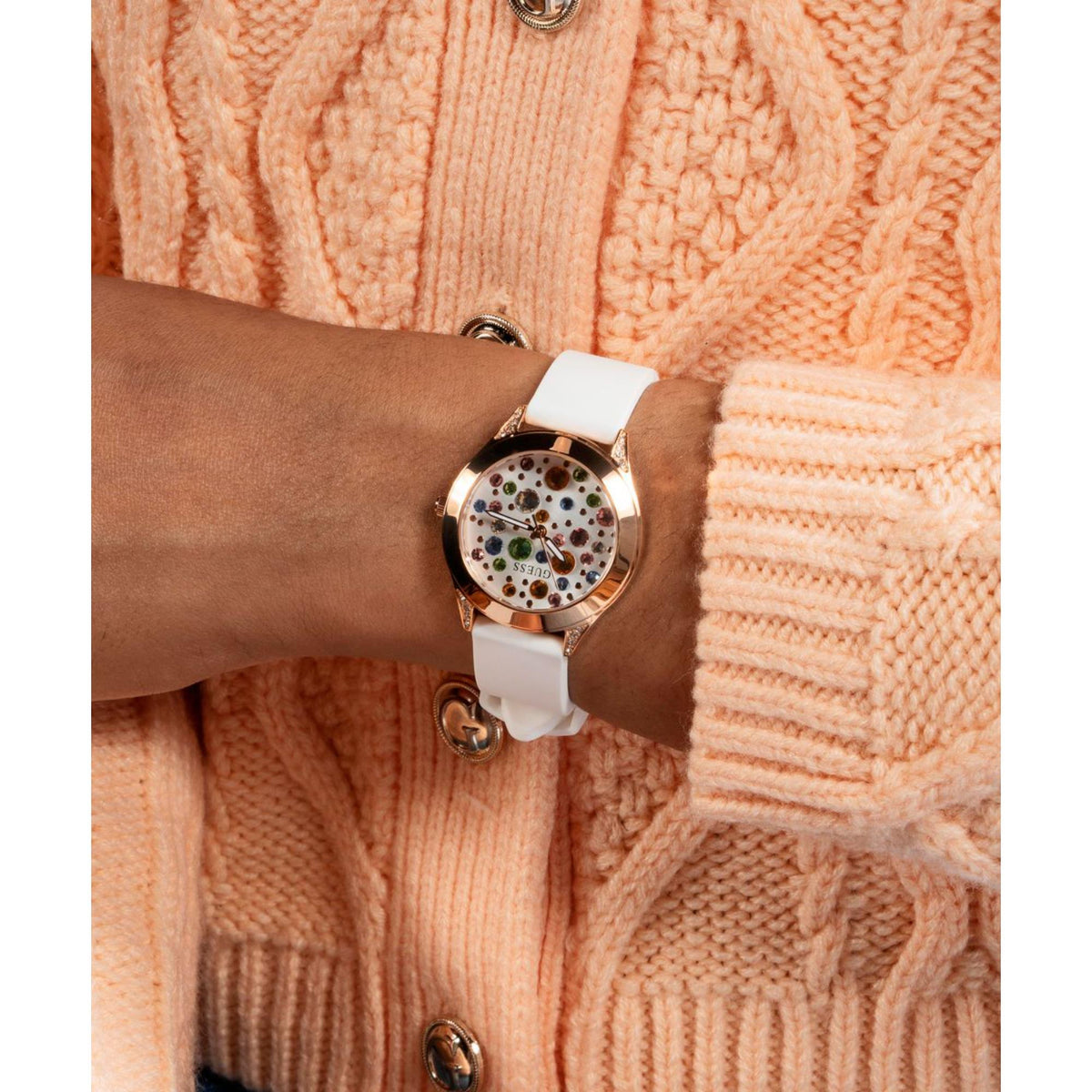 Guess watch on wrist with white silicone strap and rose-gold bezel; multicolor jeweled dial