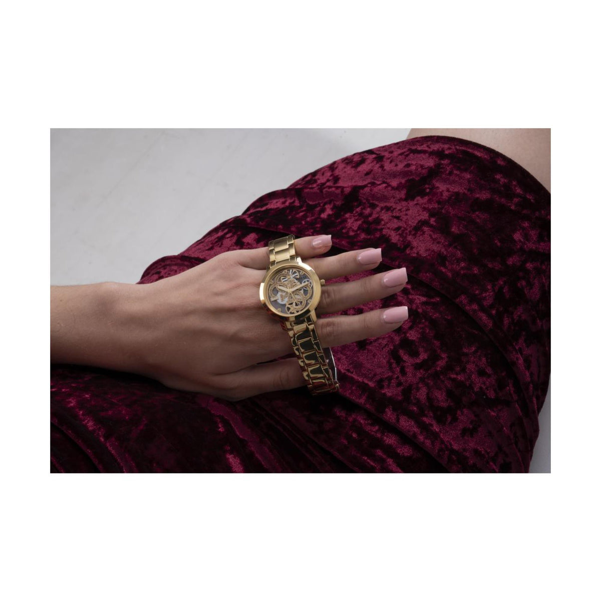 Women’s gold-tone skeleton dial watch on wrist with gold link bracelet.
