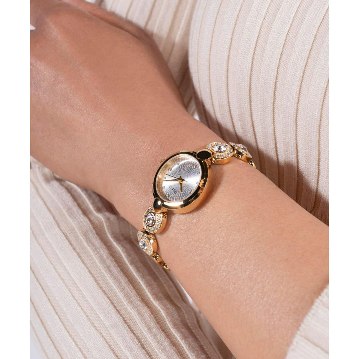 Women’s gold-tone watch on wrist with crystal crown accents and white dial