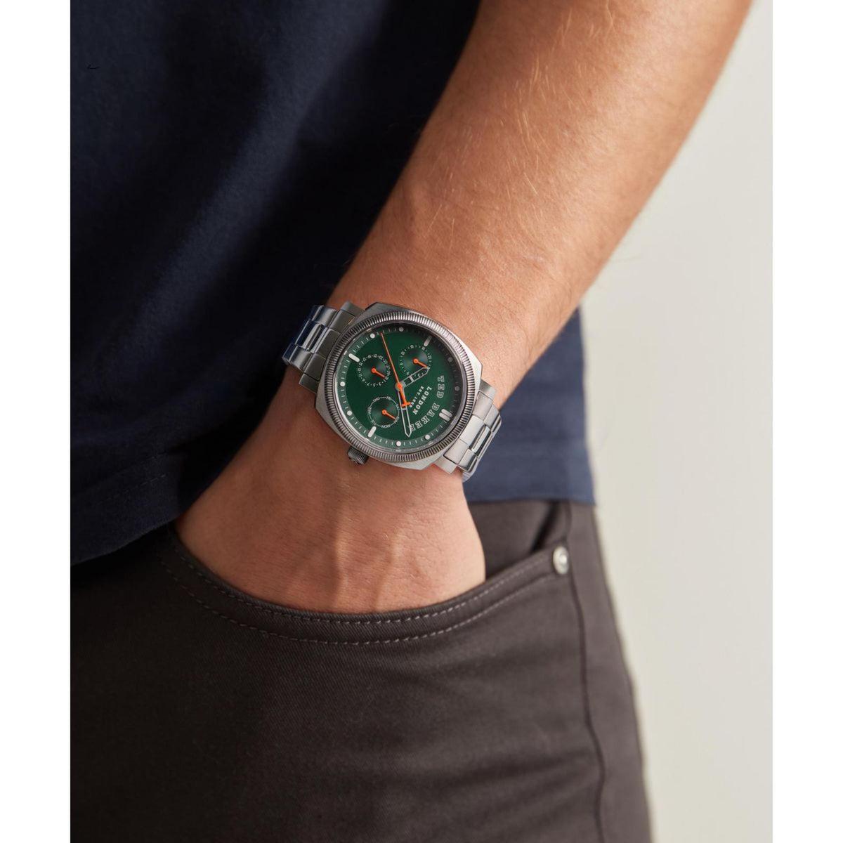 Men's stainless steel watch on wrist with green dial and orange-accent chronograph