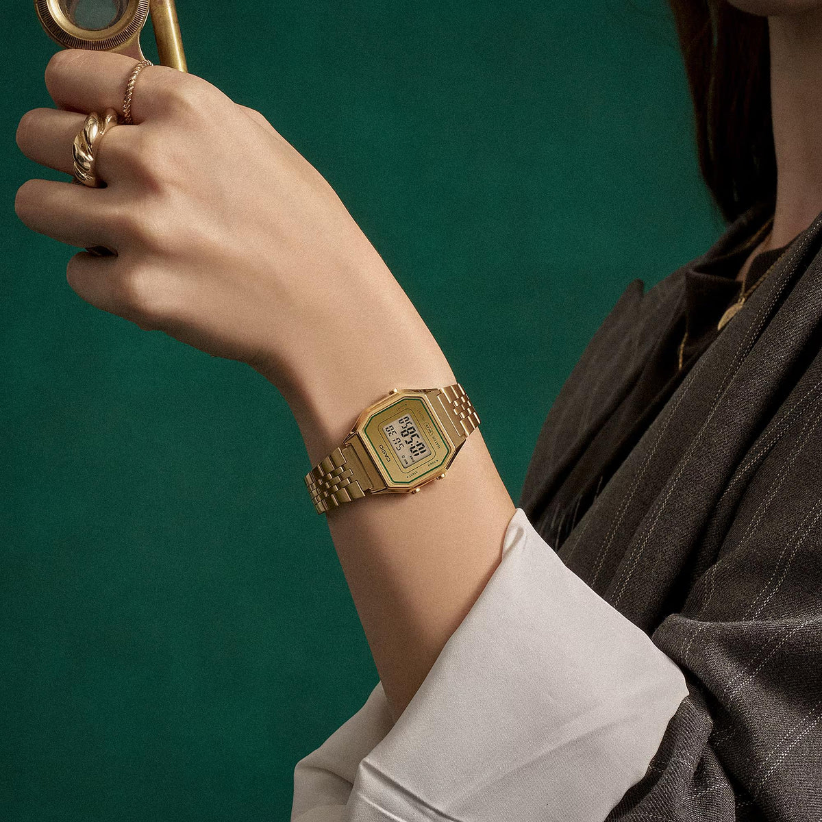 Casio Vintage LA680WEGV-9AEF on wrist against a deep green backdrop, showcasing the gold-plated steel strap and retro design