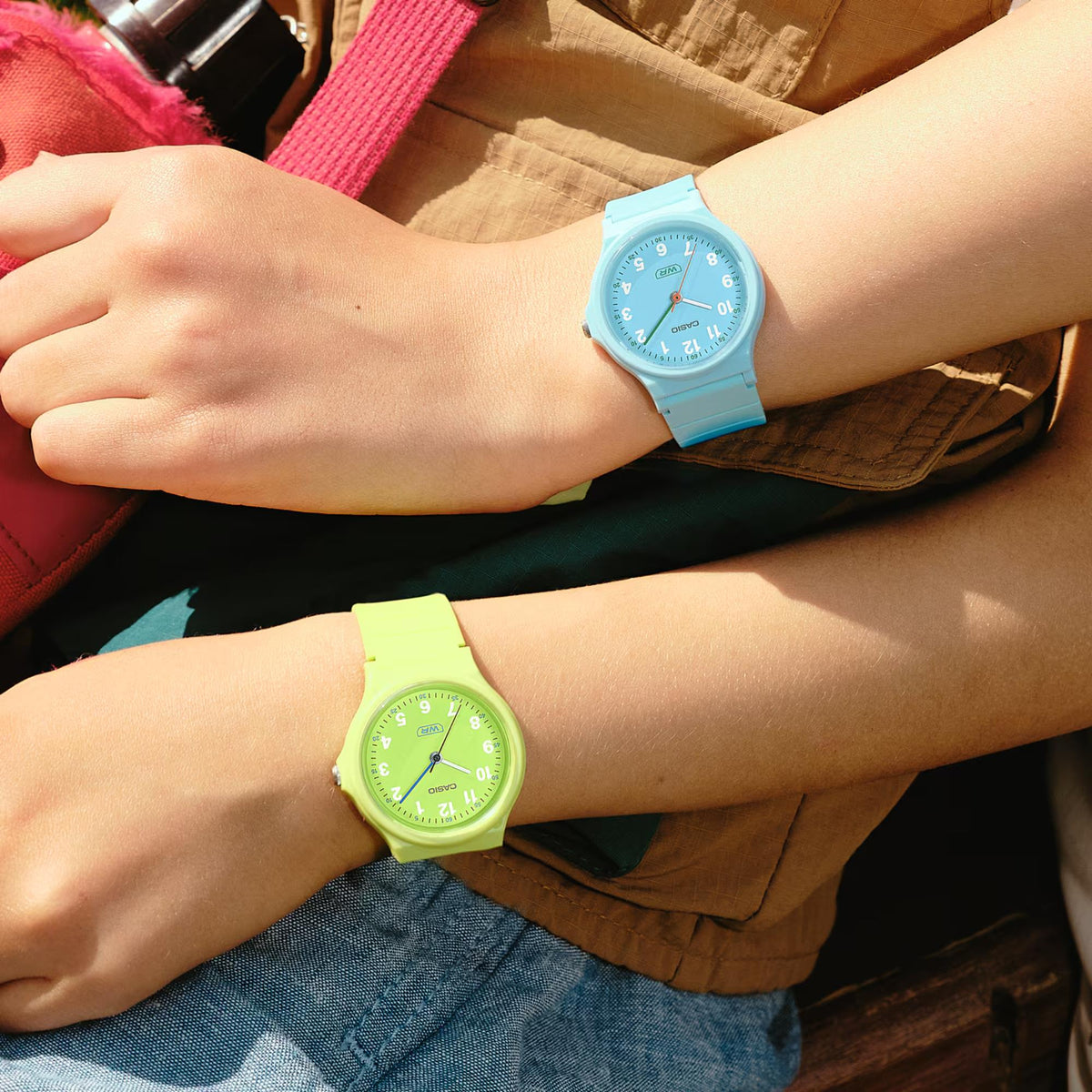 Lime green resin strap analog watch worn on wrist, beside light blue watch