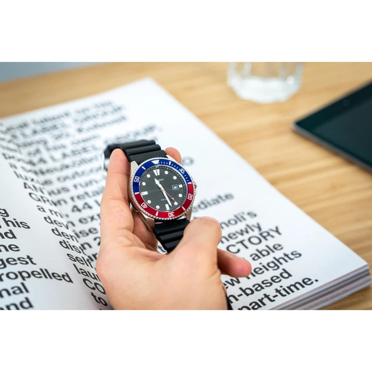 Hand holding the Casio Marlin MDV-107-1A3VEF mens watch showcasing the black resin strap and two-tone bezel over printed paper
