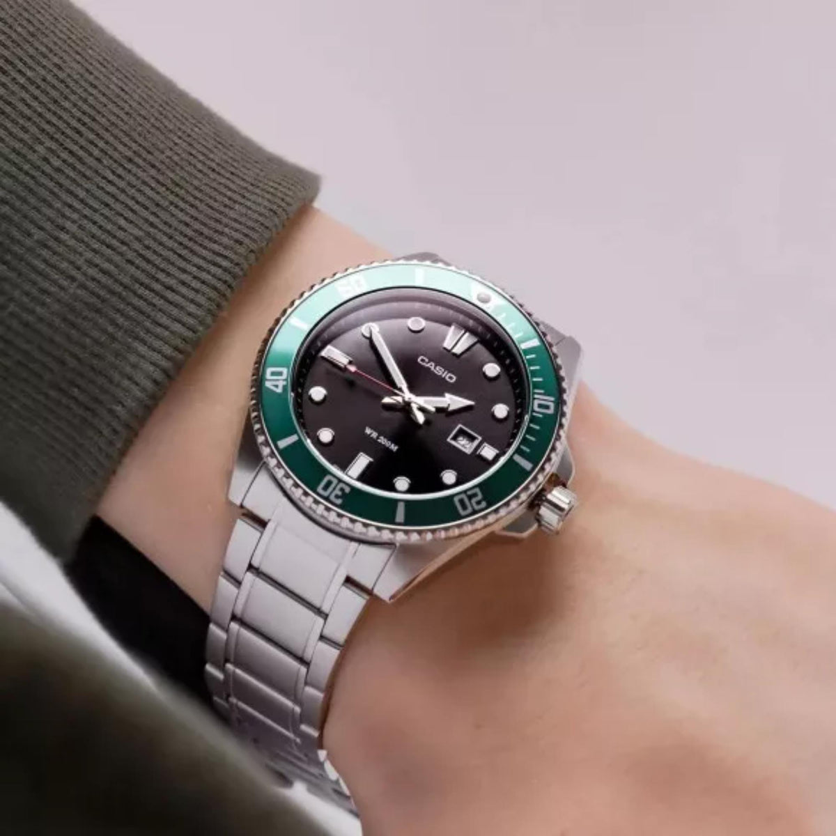 Casio men's stainless steel watch on wrist with green bezel and black dial, metal band