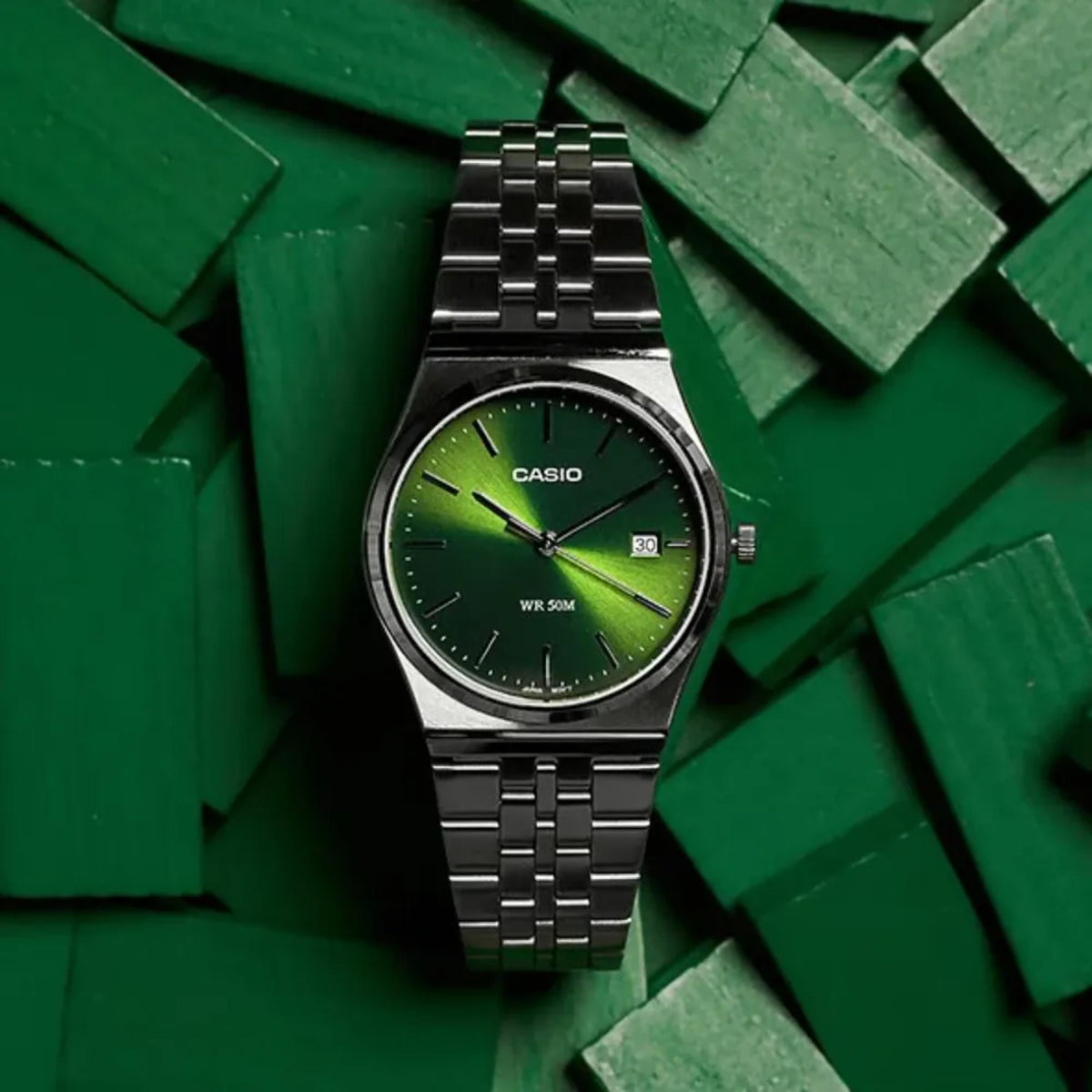 Close-up shot of the Casio MTP Series MTP-B145D-3AVEF men's analog watch with a green dial, set against a dark green wooden block background