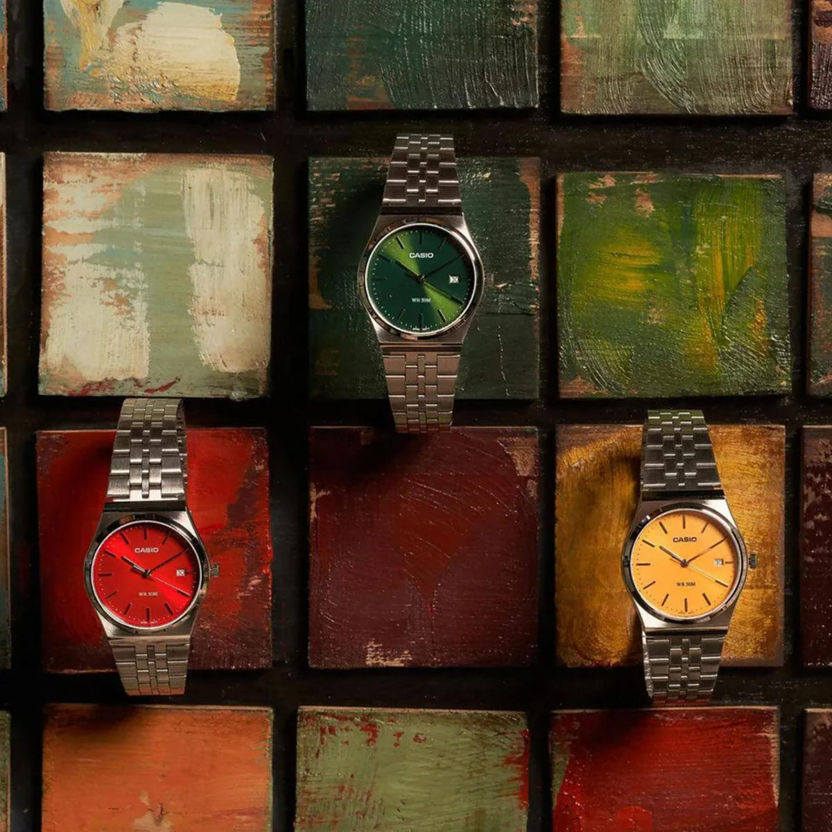Casio MTP Series MTP-B145D-3AVEF green dial mens stainless steel watch displayed alongside red and yellow dial variations on a multi-colored background