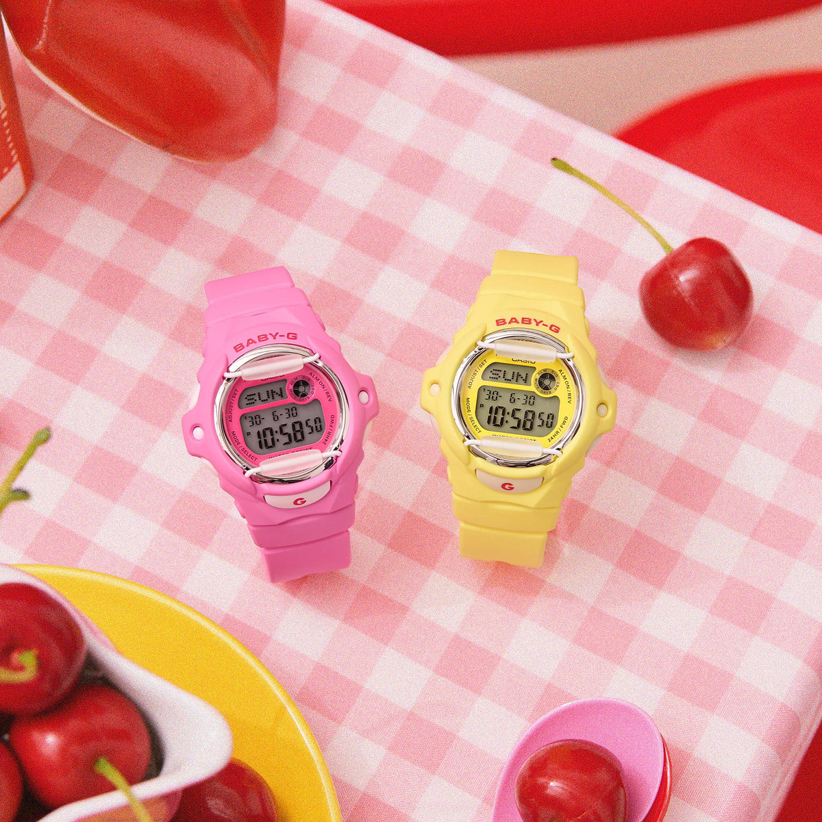 Pink Casio BABY-G digital watch beside yellow resin strap watch on table.