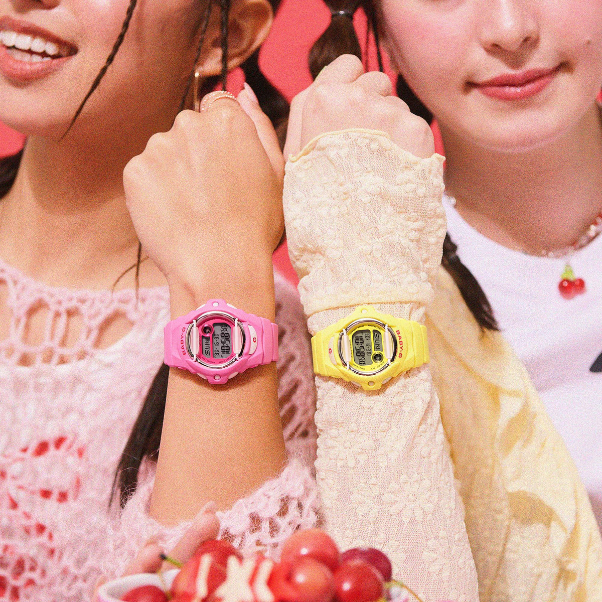 Pink and yellow Casio BABY-G digital watches on wrists, round LCD faces.
