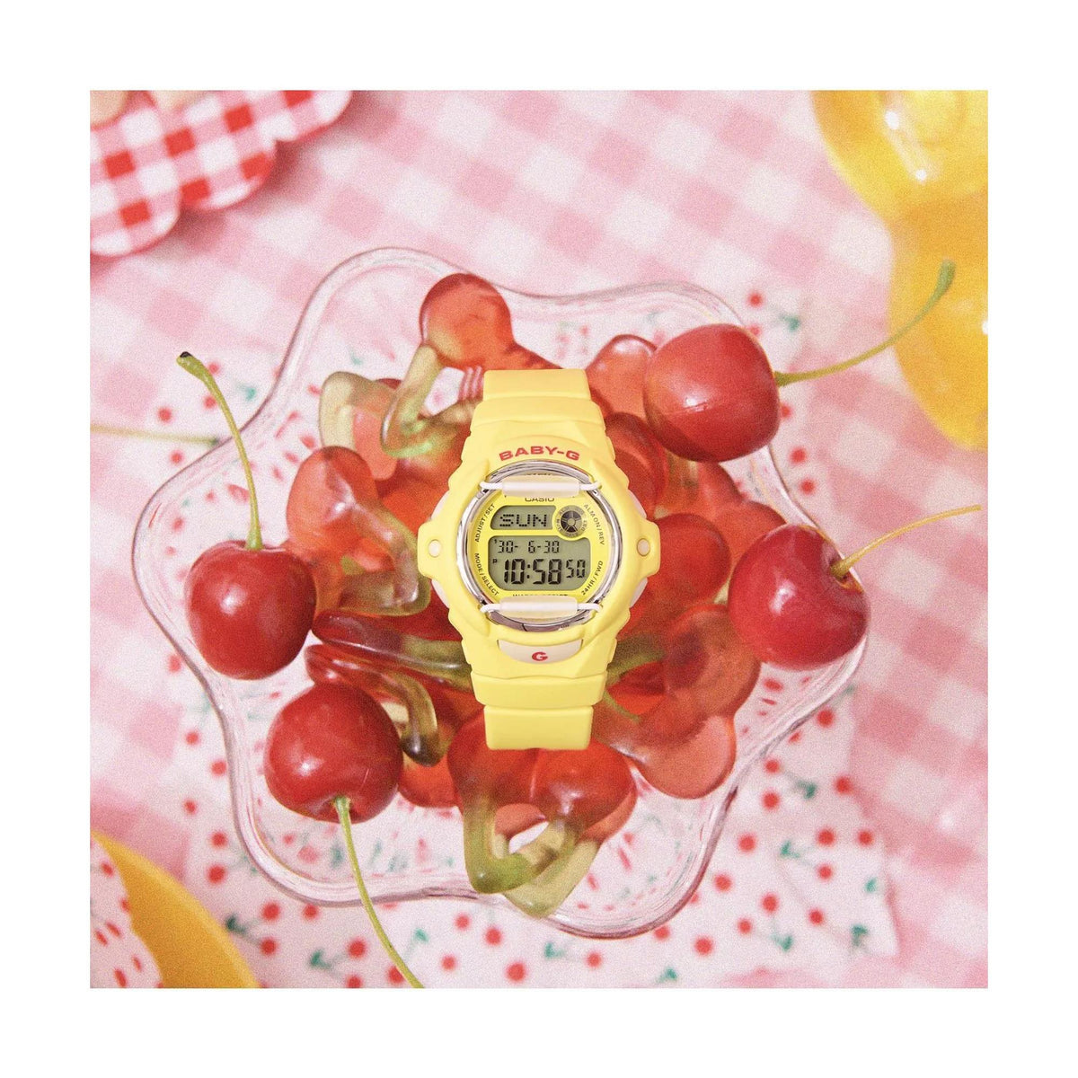 Top-down view of the Casio Baby-G BG-169CH-9ER digital watch resting in a glass bowl with fresh cherries