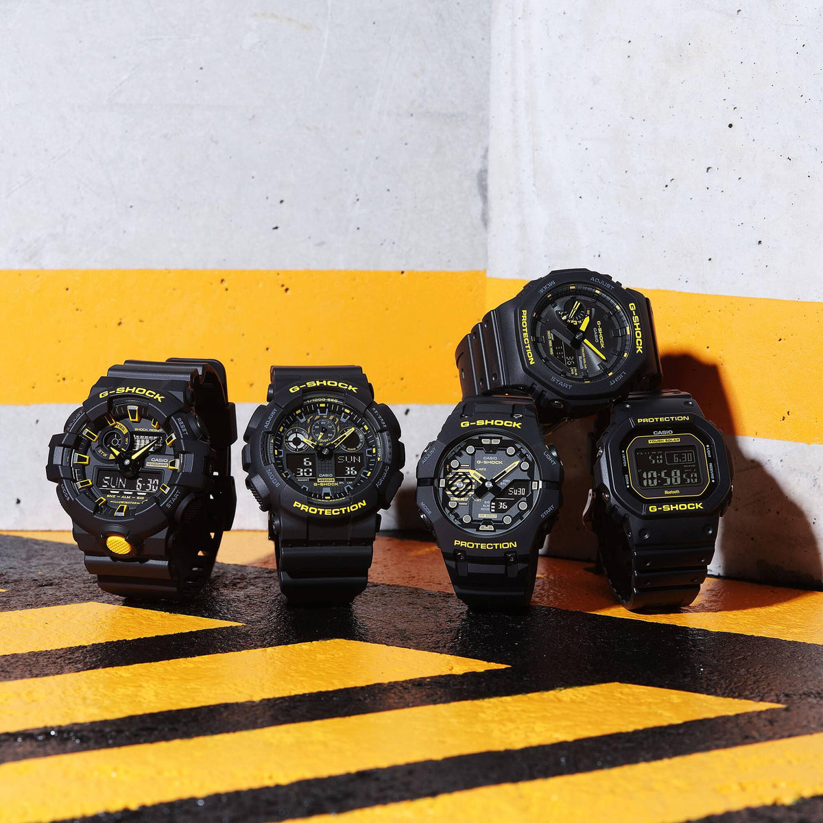 Group of four black G-Shock digital watches with yellow-accented dials on the ground.