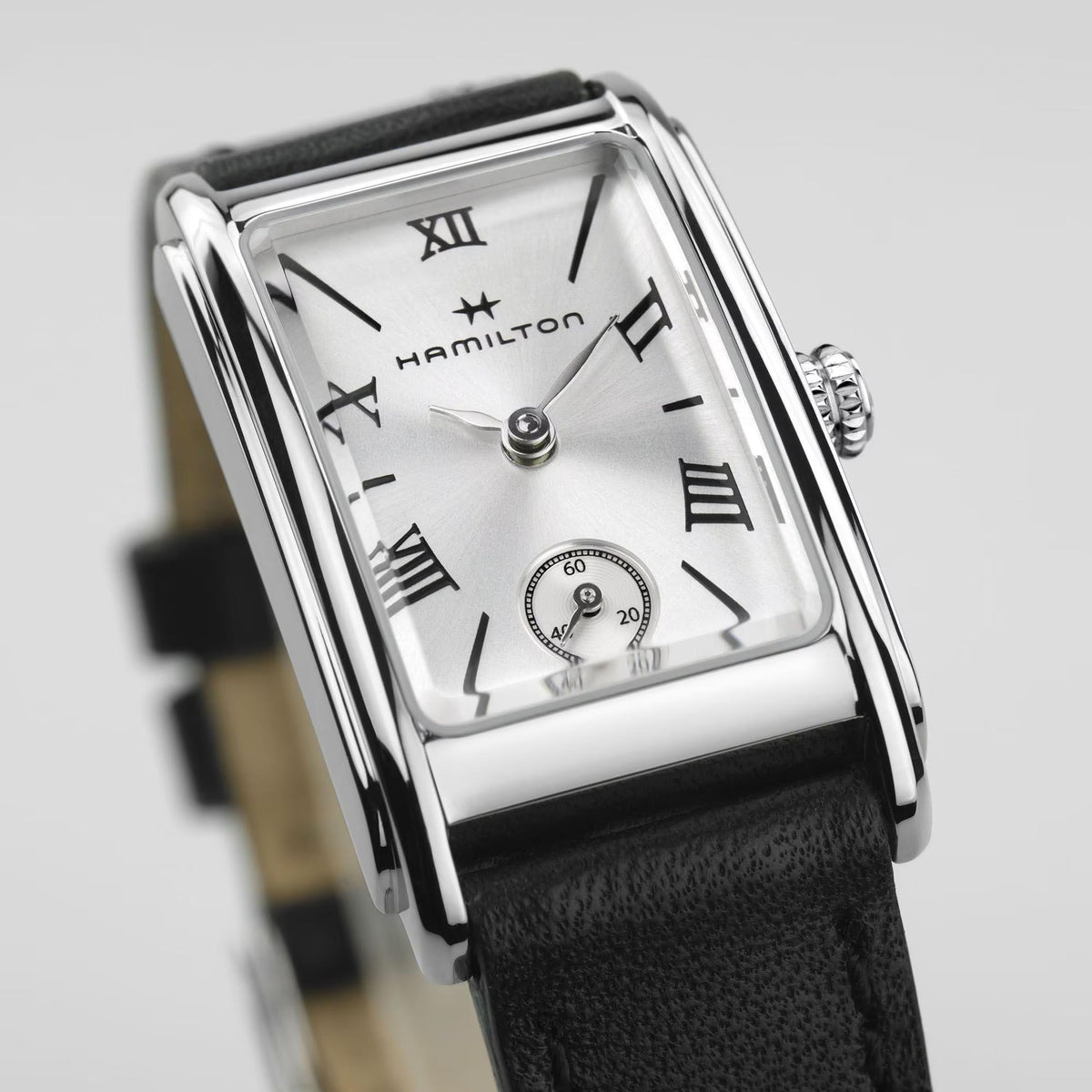 Ladies quartz watch close-up with silver case, white dial, roman numerals, and black leather strap.