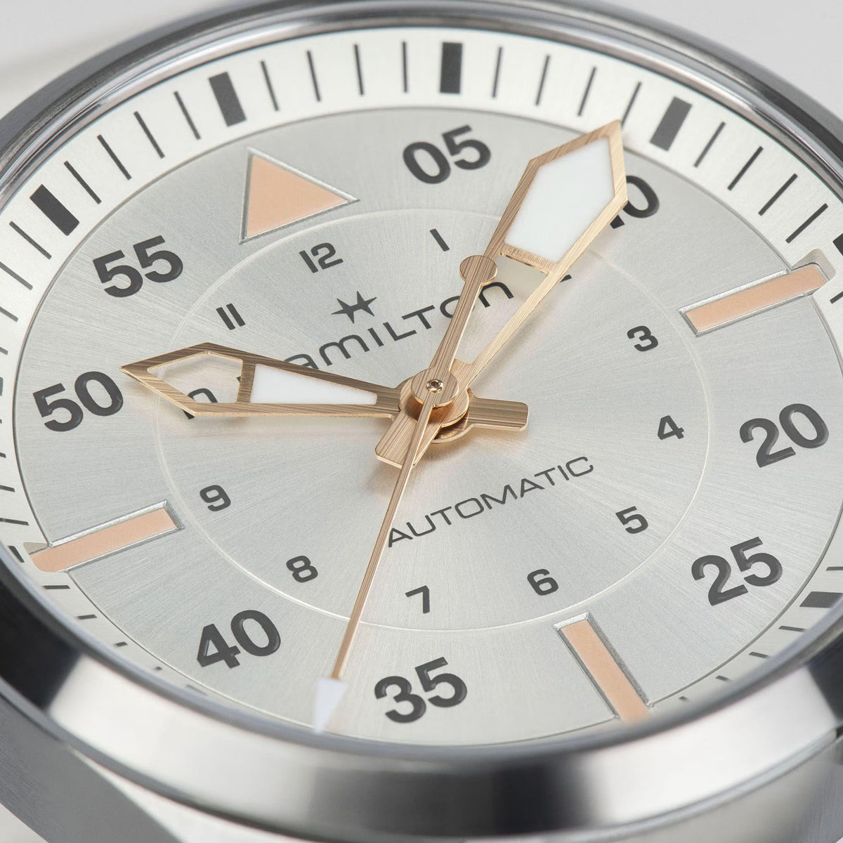 Round dial closeup with light gray face, gold-tone hands, and minute markers