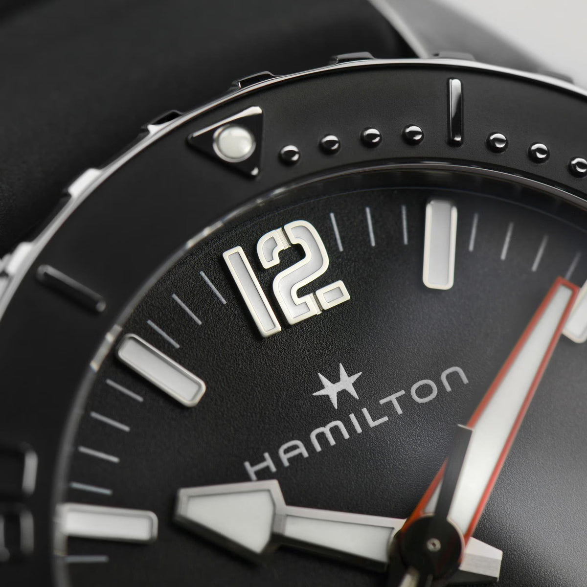 Close-up of black dial automatic watch with Hamilton logo, indices, and orange accents