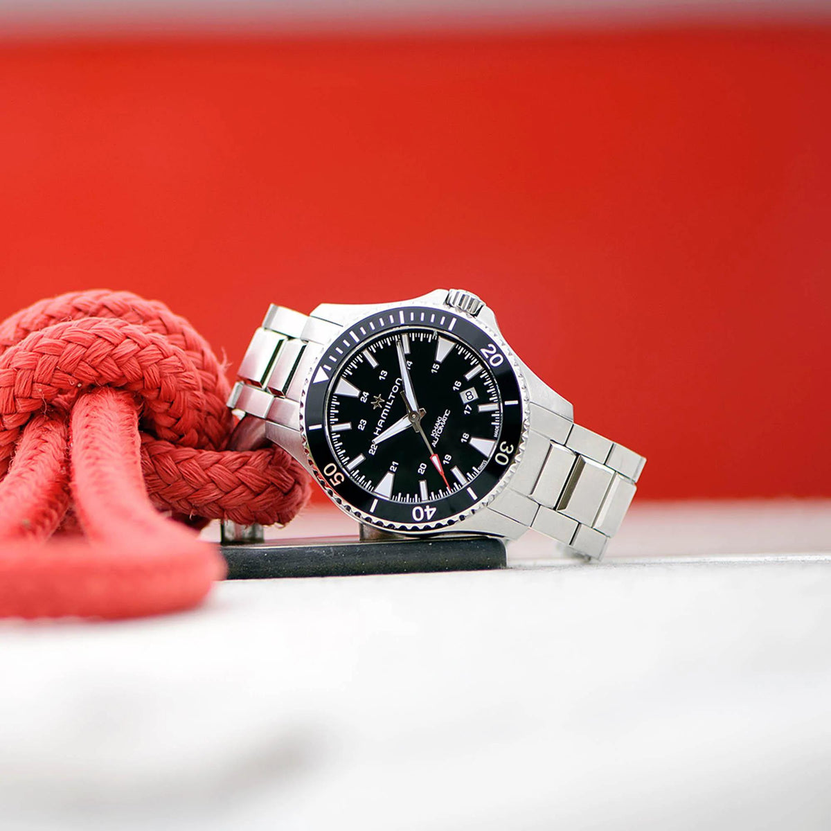 Hamilton Khaki Navy H82335131 steel divers watch resting beside a coiled red nautical rope.