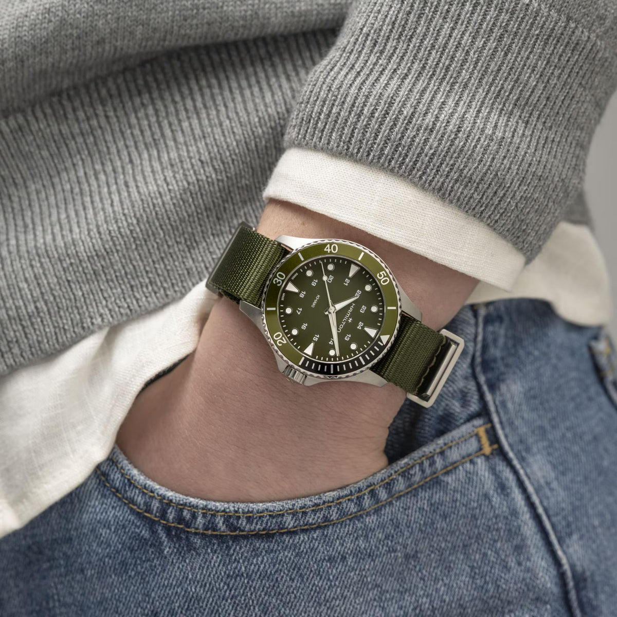 Hamilton watch with green dial and olive NATO strap on wrist, round steel case.