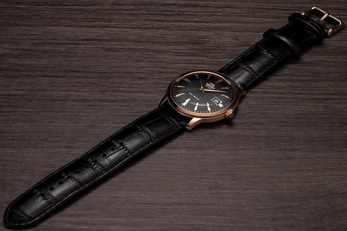 Men's automatic wristwatch on black leather strap, rose-gold case, crown at side.