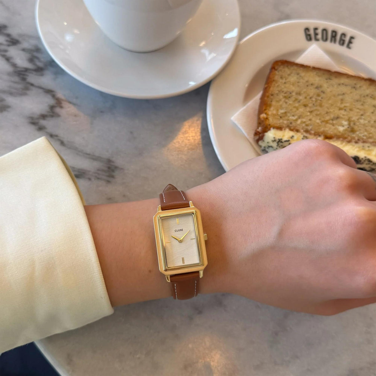 Women's gold rectangular watch with white dial and brown leather strap on wrist