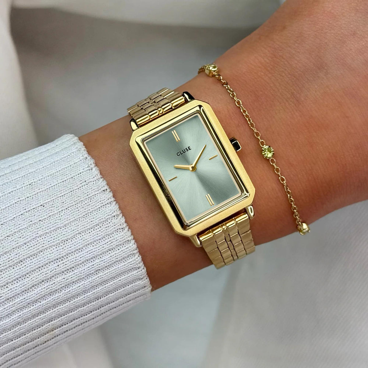 Women's rectangular gold-tone steel watch with green dial and metal bracelet on wrist